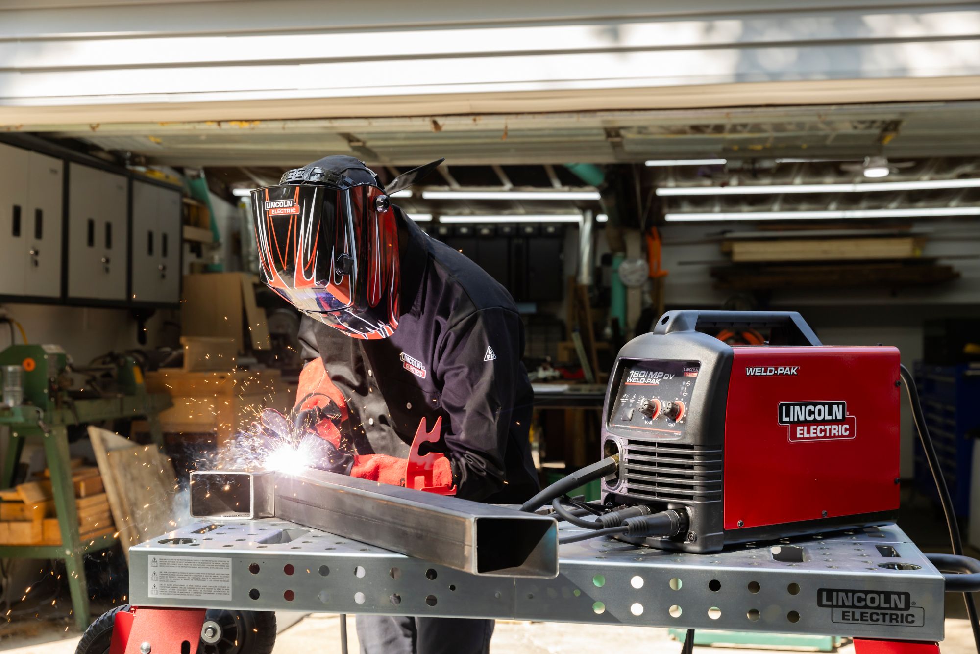 Person welding metal with a Lincoln Electric machine in a workshop.