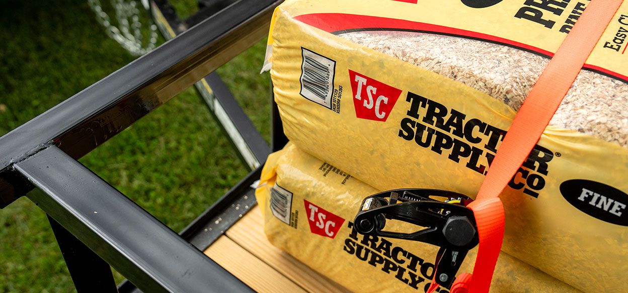 Bulk feed bags stacked in a Tractor Supply shopping cart.