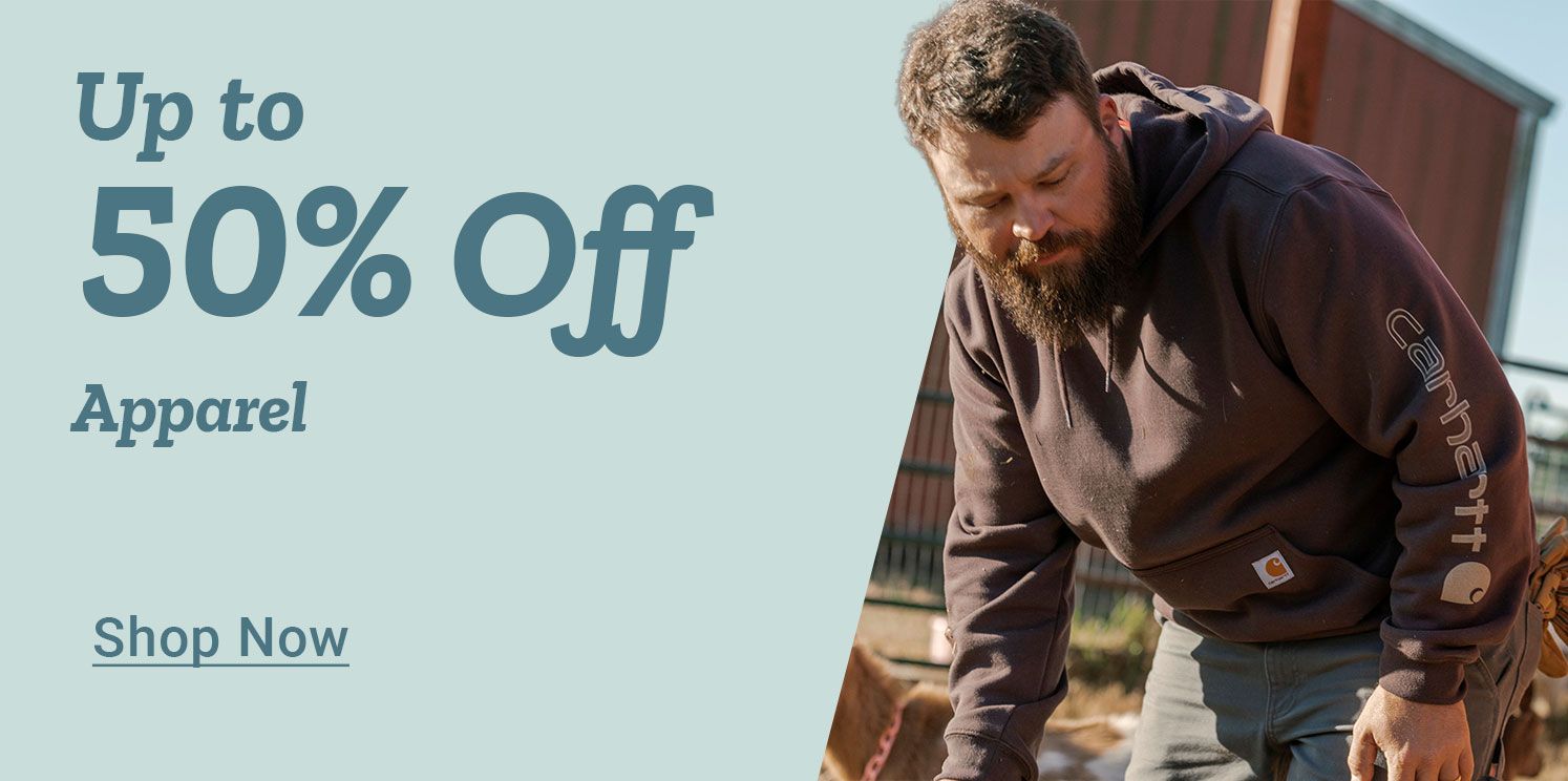 Promotional banner advertising a seasonal sale. Large headline text reads: Up to 40 percent off Cold Weather Apparel &amp; Accessories. A Shop Now call to action appears below the text. On the right side of the image, a woman wearing a tan insulated work jacket, knit beanie, gloves, and jeans stands inside a barn or shed, holding a propane tank. Farming tools, shelves, and equipment are visible in the background, emphasizing cold weather workwear and accessories in a rural setting.