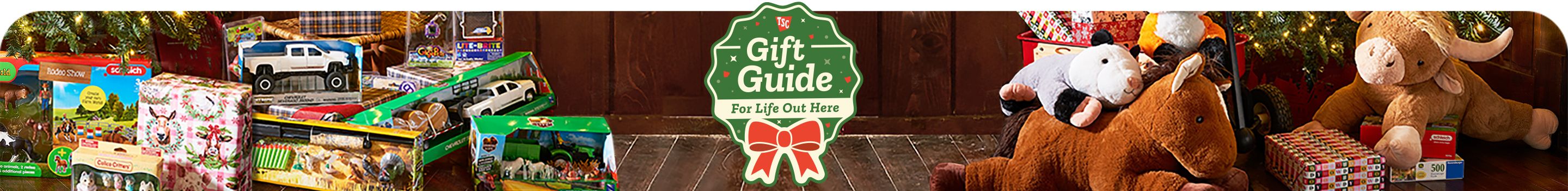 Holiday-themed promotional banner titled Gift Guide For Life Out Here featuring a green badge design with a red ribbon bow at the center. The background shows Christmas gifts under a decorated tree, including plush animals, toy trucks, and boxed toys. The warm lighting and rustic wooden floor create a cozy festive atmosphere highlighting holiday shopping ideas.
